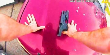 Person securing handgun on red car hood.