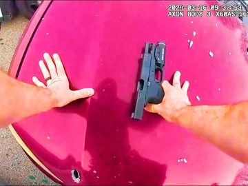 Person securing handgun on red car hood.