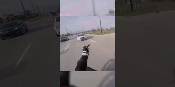 Motorcyclist gestures at police car on road.