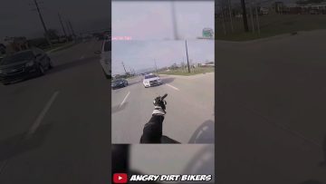 Motorcyclist gestures at police car on road.