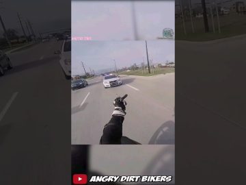 Motorcyclist gestures at police car on road.