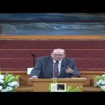 Man speaking at a church podium with flowers.
