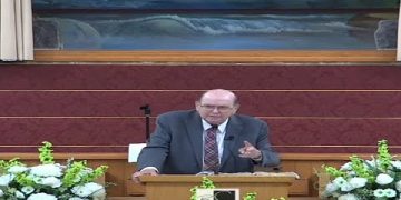 Man speaking at a church podium with flowers.