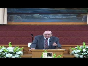 Man speaking at a church podium with flowers.