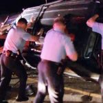 Police officers flip overturned car during night operation.