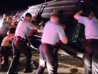 Police officers flip overturned car during night operation.