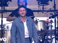 Musician performing on stage with drums behind.