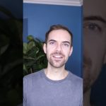 Person smiling in front of blue wall and plant.