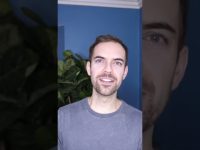 Person smiling in front of blue wall and plant.