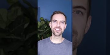 Person smiling in front of blue wall and plant.