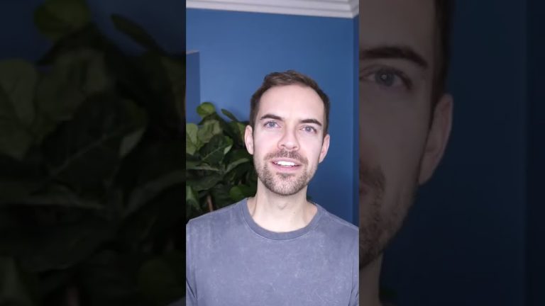 Person smiling in front of blue wall and plant.