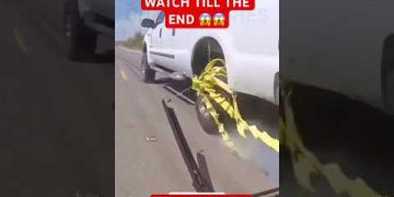 Truck wheel tangled in yellow tape on road.