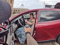 Officer pointing Taser at woman in red car.