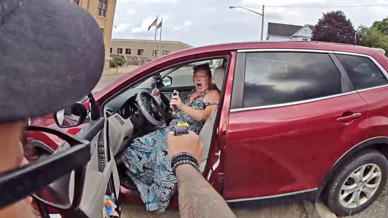 Officer pointing Taser at woman in red car.