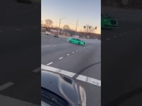 Green car drifting on a wide intersection road.