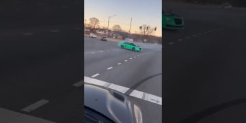 Green car drifting on a wide intersection road.