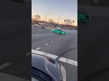 Green car drifting on a wide intersection road.