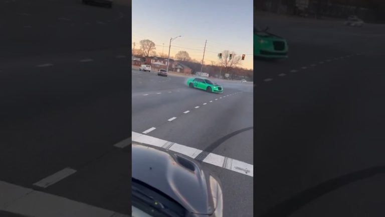 Green car drifting on a wide intersection road.