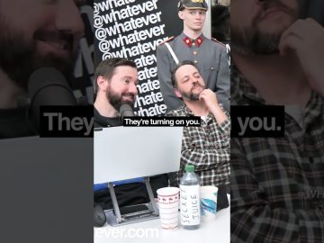 Two men with microphones and soldier prop behind.