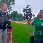 Police officer interacts with person in green shirt.
