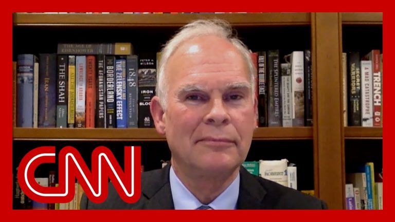 Man in suit with bookshelf background, CNN logo overlay.