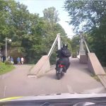 Motorcyclist crossing park bridge on sunny day.