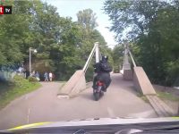 Motorcyclist crossing park bridge on sunny day.