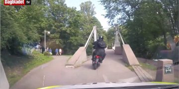 Motorcyclist crossing park bridge on sunny day.