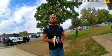 Person eating banana near police car and tents.