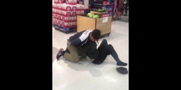 Security tackle in supermarket near bottled drinks display.
