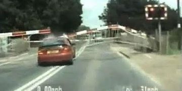 Car crossing railway tracks under lowering barriers.