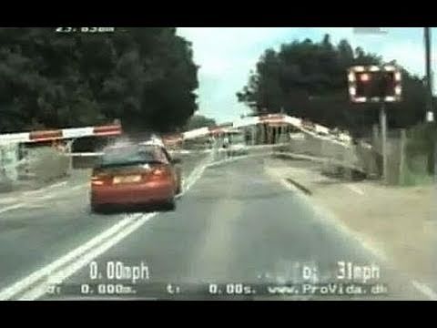 Car crossing railway tracks under lowering barriers.