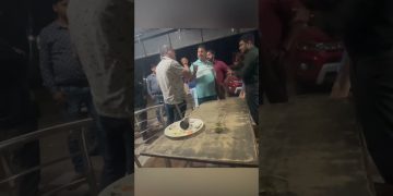 Group of men arguing near a table at night.
