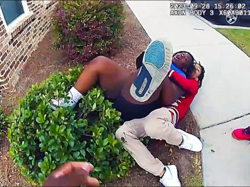 Two people wrestling on the ground near sidewalk.