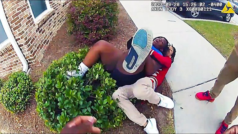 Two people wrestling on the ground near sidewalk.