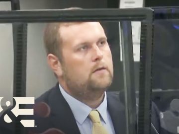 Man in suit behind glass at a desk.