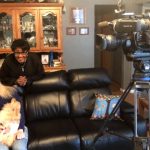 Women and dog seated, filmed by camera crew.