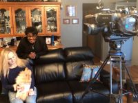 Women and dog seated, filmed by camera crew.