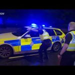 Police officers respond with patrol car at night.