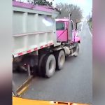 Pink dump truck on road, shot from vehicle dashboard.