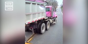 Pink dump truck on road, shot from vehicle dashboard.
