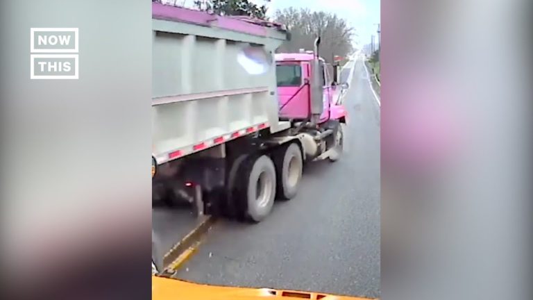 Pink dump truck on road, shot from vehicle dashboard.