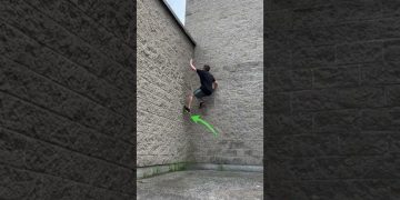 Person climbs brick wall using parkour technique.
