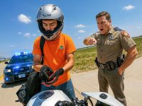 Police officer stops motorcyclist on highway.