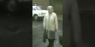 Woman in street near parked white car.