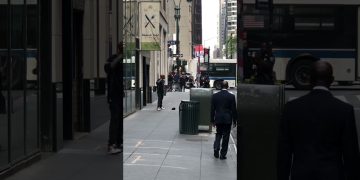 Man walks on busy city sidewalk, police nearby.