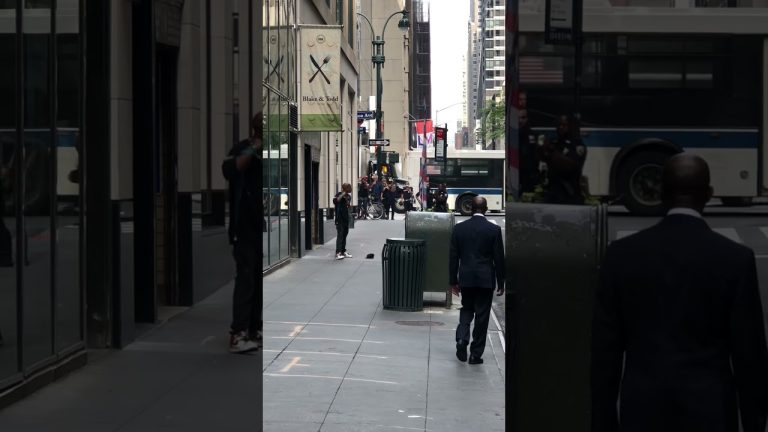 Man walks on busy city sidewalk, police nearby.