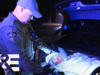 Police officer inspecting car trunk at night.