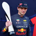 Racing driver holds a unique trophy on podium.