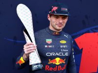 Racing driver holds a unique trophy on podium.
